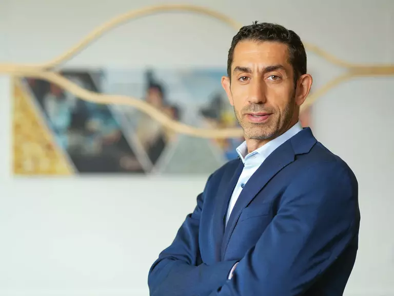 Portrait of Rakan Rahbani in a blue suit and light blue shirt with his arms crossed