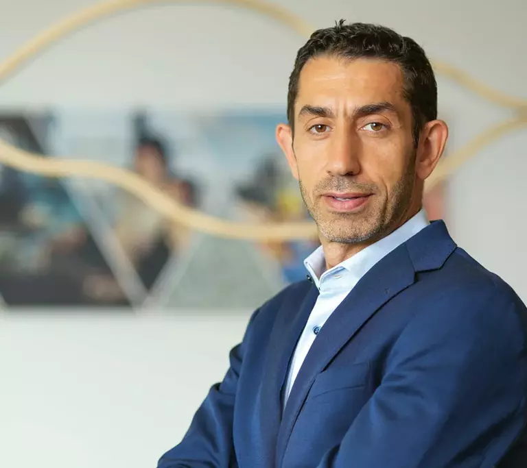 Portrait of Rakan Rahbani in a blue suit and light blue shirt with his arms crossed