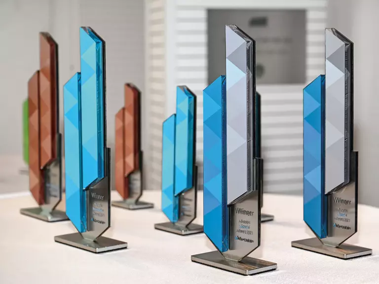 Several Aurubis Awards in different colours (blue, grey, red) standing next to each other on a table.