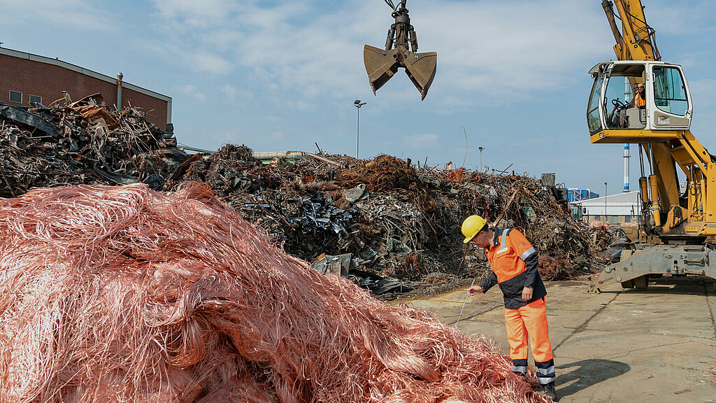 An excavator shovel lowering onto a pile of scrap metal