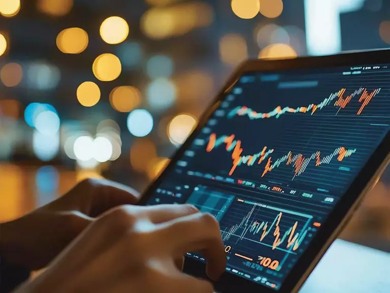 Black screen showing green and red graphs, with hands typing below, background blurred.