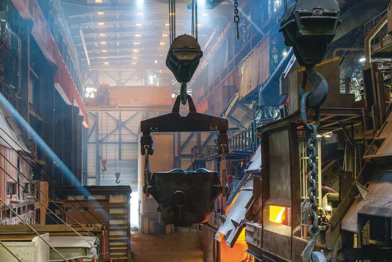 The interior of a smelting hut at the Aurubis east plant, with a crane in the centre, a factory hall in the background and a melting pot on the right