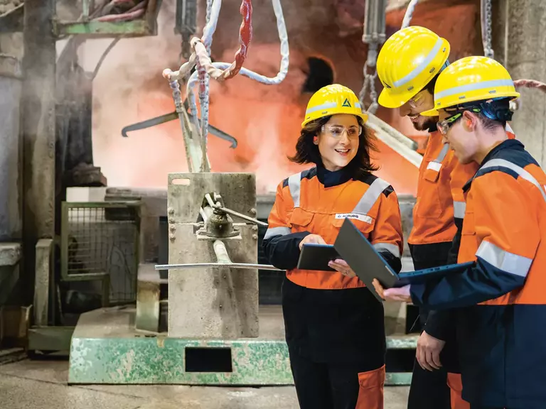 Two men and a woman at work in orange safety clothing with yellow helmets, safety goggles and folders in their hands