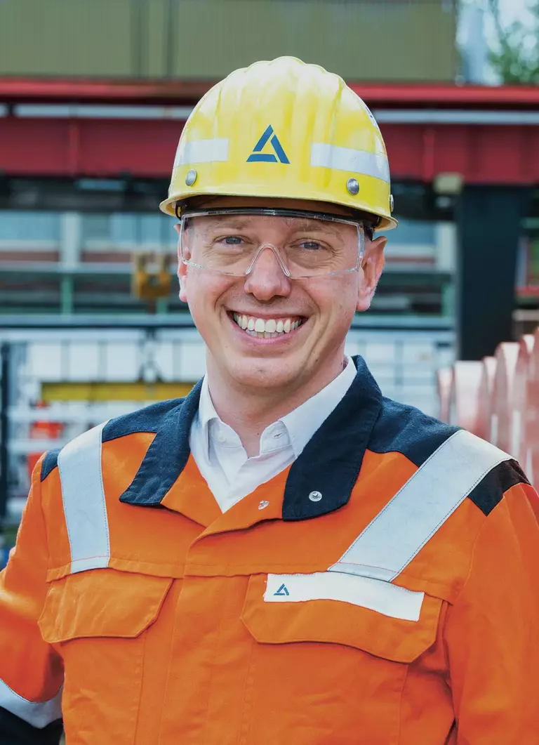 Construction worker wearing a yellow safety helmet with the Aurubis logo and an orange high-visibility jacket
