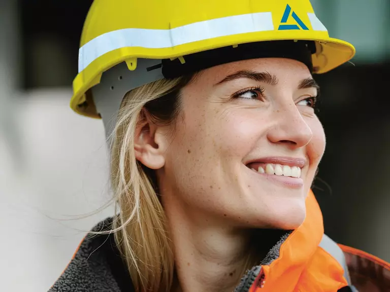 Young woman working at Aurubis with blonde hair, orange high-visibility jacket and yellow construction helmet