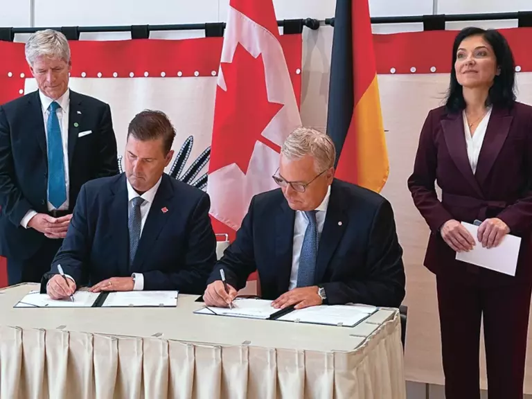 Signing of the Memorandum of Agreement between Aurubis and Troilus Gold Corp. The photo shows two men in suits sitting down and signing, flanked by a woman and another man.