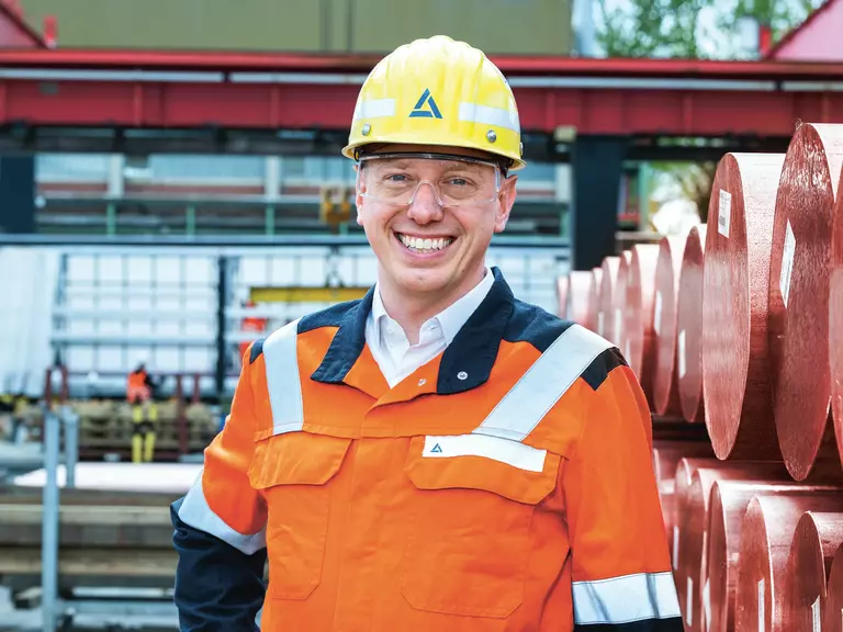 Construction worker wearing a yellow safety helmet with the Aurubis logo and an orange high-visibility jacket