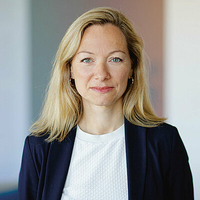 Portrait of Anne Lauenroth, Deputy Head of the Department for International Cooperation, Security, Raw Materials and Space, Bundesverband der Deutschen Industrie e. V., wearing a blue blazer, white top and shoulder-length blonde hair