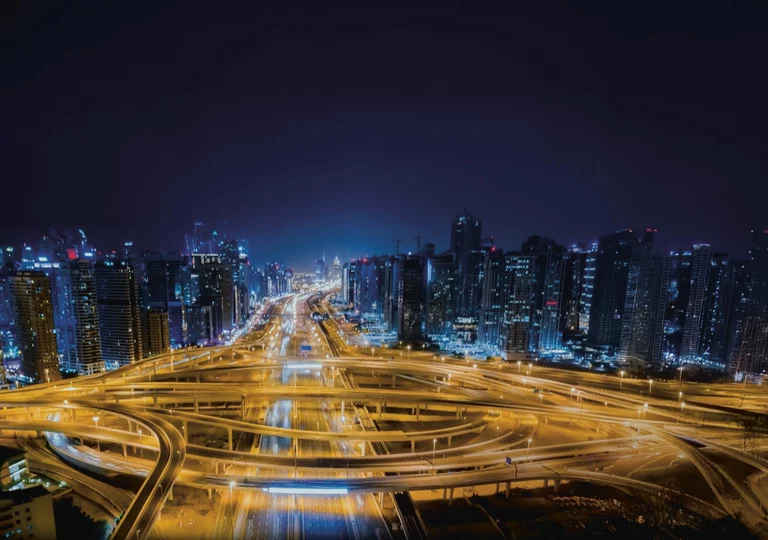 Skyline of a large city at night, with an empty network of streets illuminated by warm lantern light in the foreground