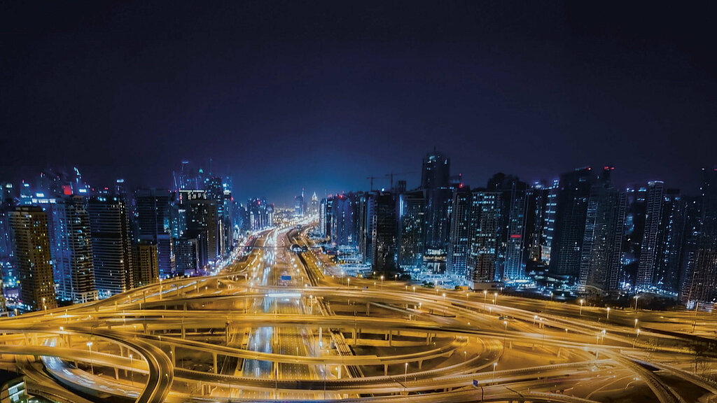 Skyline of a large city at night, with an empty network of streets illuminated by warm lantern light in the foreground