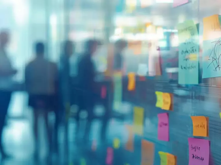 Wall with colourful Post-it notes on the right-hand side, blurred background showing an office with employees