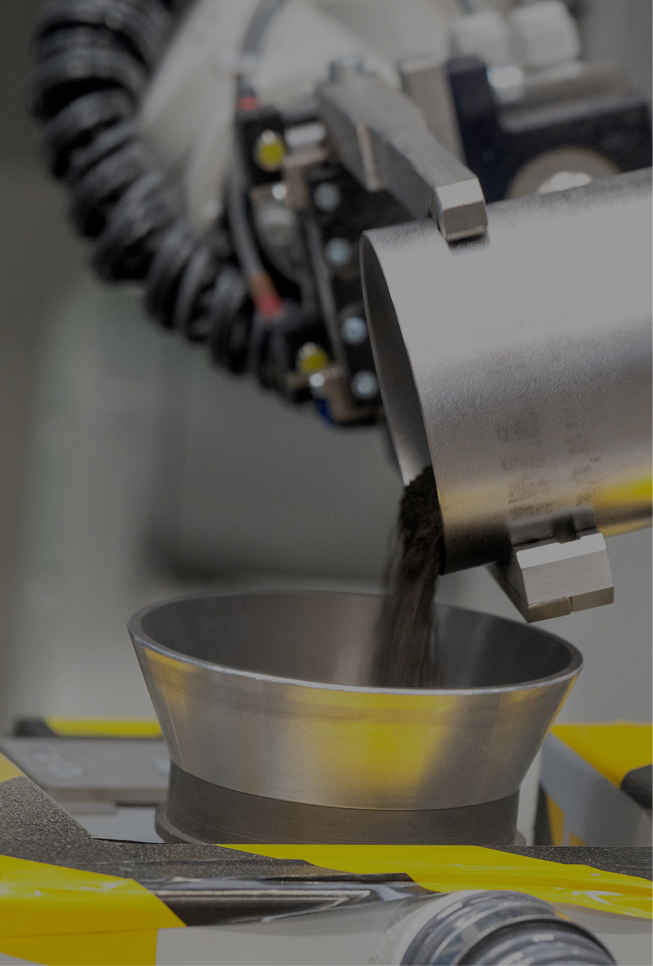 Fourth level of Aurubis Performance 2030: Innovation. A metal machine is shown pouring metal granulate into a device.