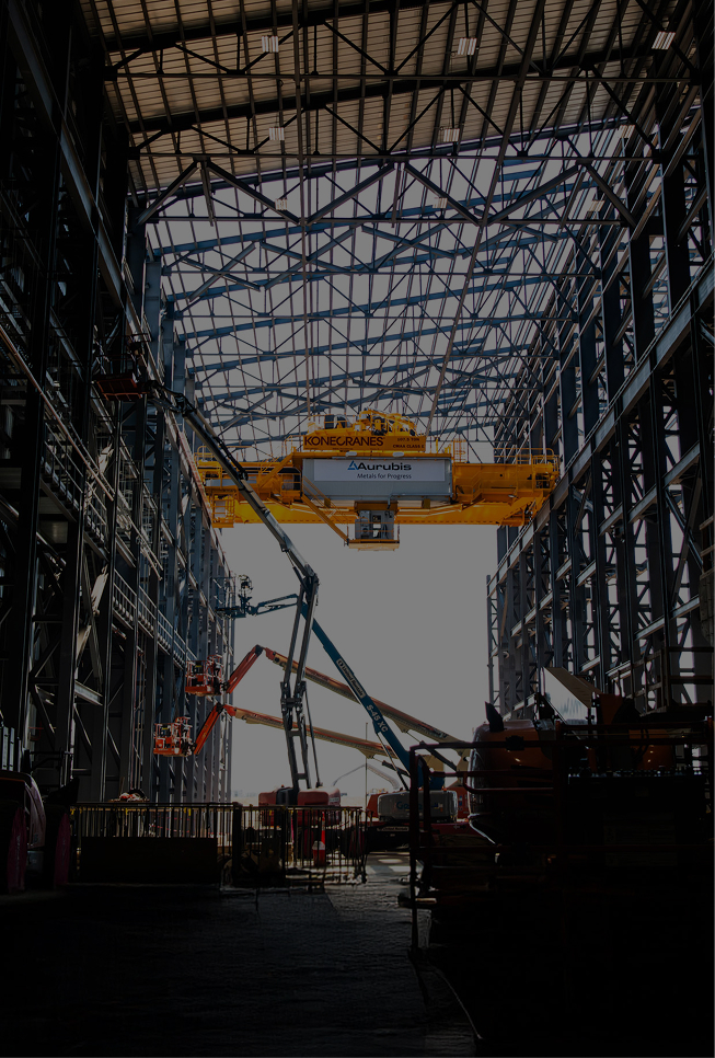 ifth level of Aurubis Performance 2030: Focused Growth. The image shows a huge warehouse with several lifting platforms and crates piled up in the background.